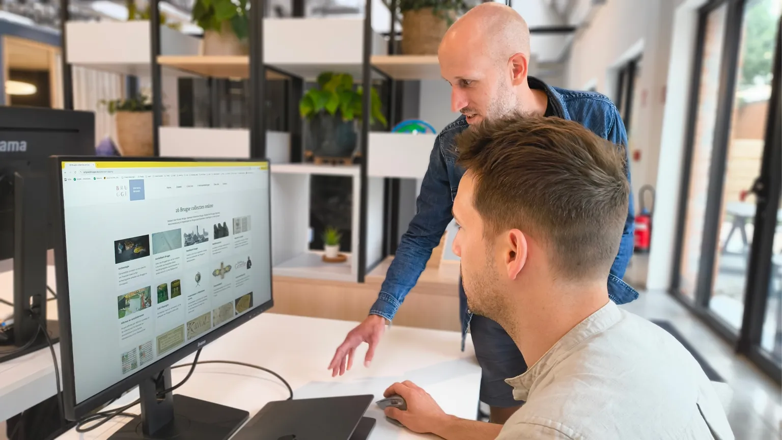 Twee Octoo-collega's overleggen geconcentreerd aan een bureau, met groene planten op de achtergrond