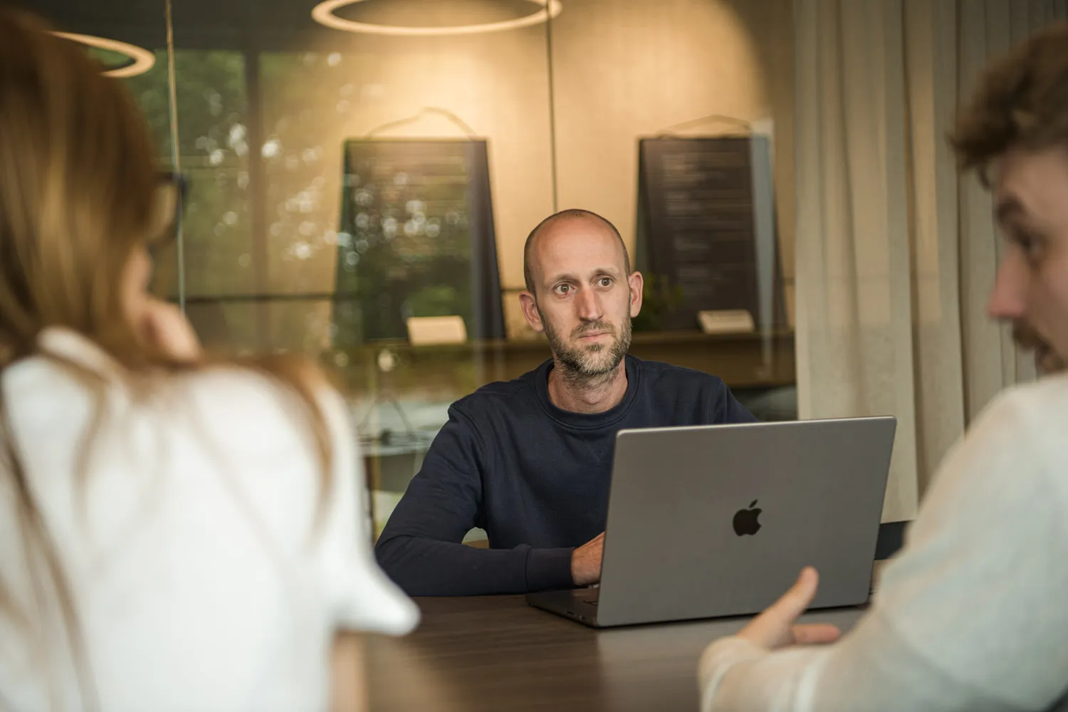 Een collega luistert aandachtig tijdens een overleg aan tafel, laptop voor zich