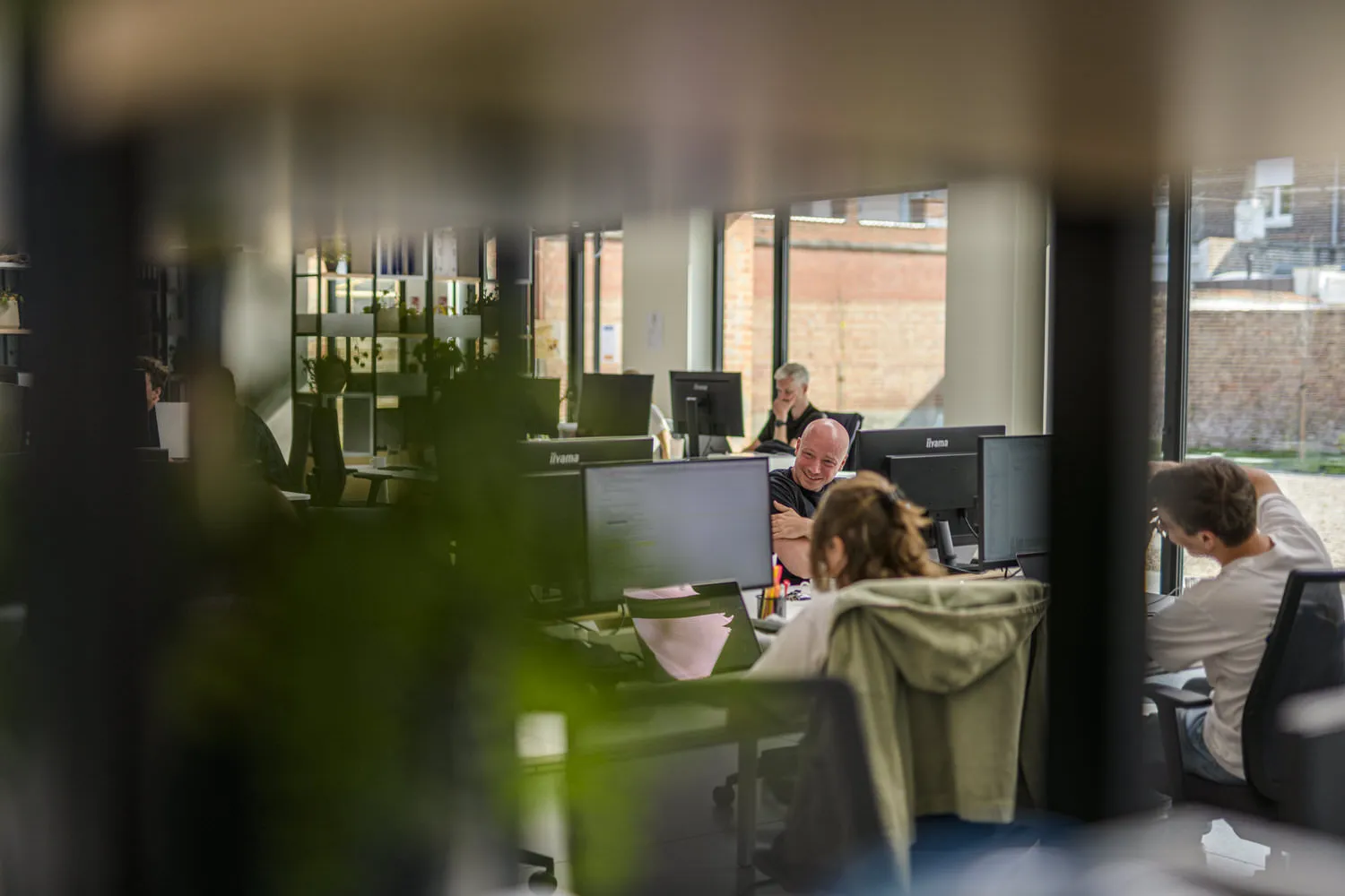 Een inkijk in het Octoo-kantoor: collega's werken aan hun bureau, een van hen lacht tijdens een gesprek