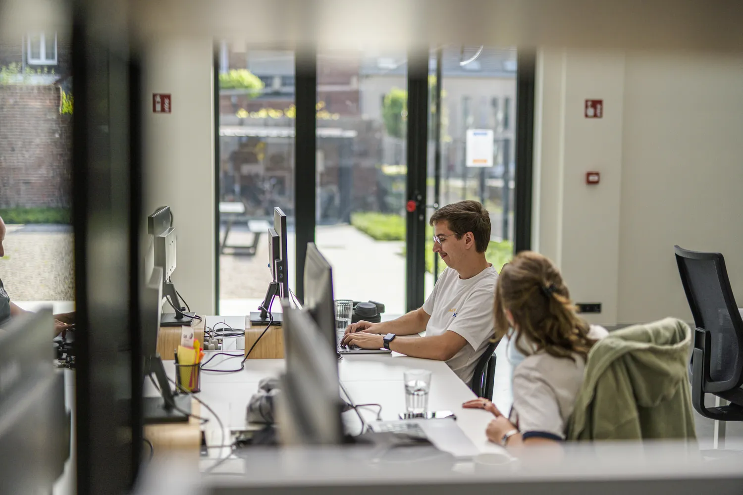 Twee collega's werken naast elkaar aan hun bureau in een licht kantoor